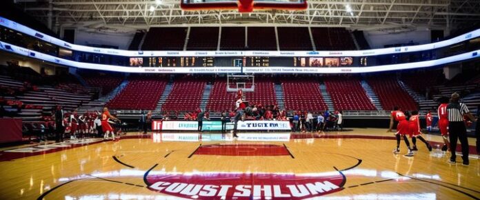 A basketball court with a crowd of people and players in red uniforms.
