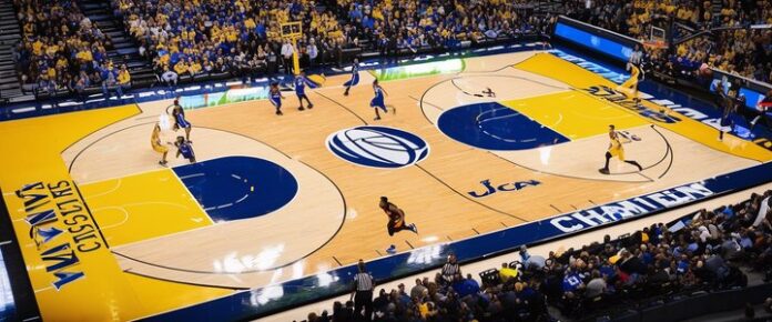 A basketball game is being played on a yellow and blue court with a crowd of spectators.