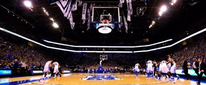 A basketball team in white uniforms on a court, with a crowd of spectators in the background.