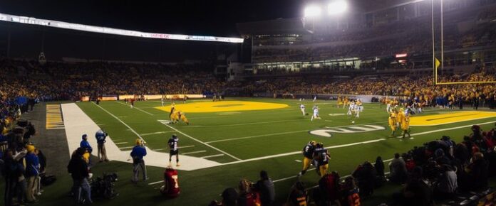 A football field with players in action, surrounded by spectators in a stadium.