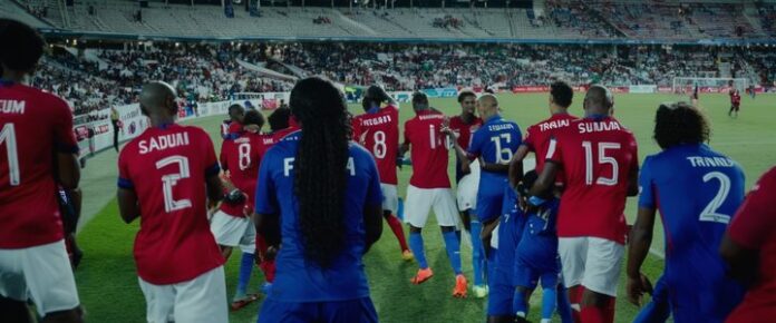 A group of soccer players, both men and women, standing on a field in front of a crowd.