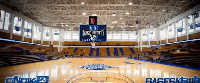 A_large_indoor_basketball_court_with_a_high_ceiling_and_bleachers_featuring_a_Duke_University_logo A large indoor basketball court with a high ceiling and bleachers, featuring a Duke University logo.