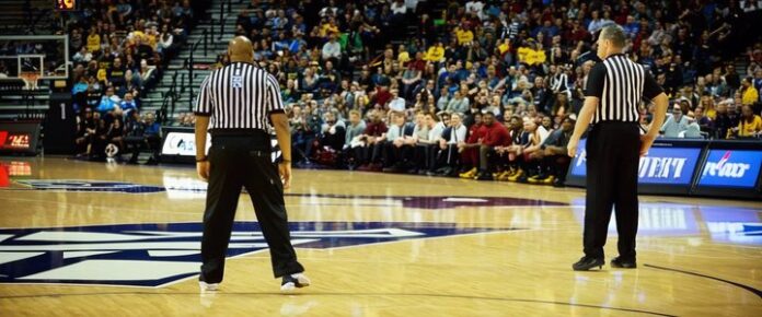 Four referees standing on a basketball court, facing a crowd of spectators.