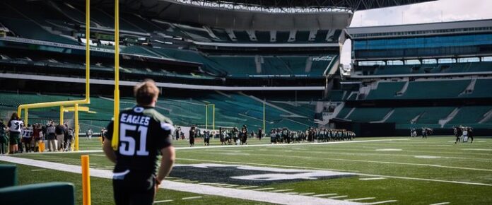 Two men in black Eagles jerseys standing on a football field with goalposts and a crowd in the background.