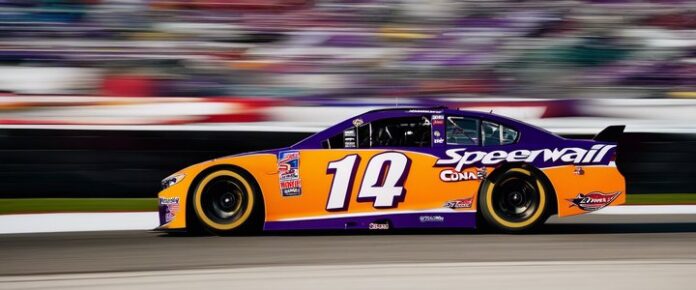 Denny Hamlin speaking at a NASCAR press conference, looking frustrated.